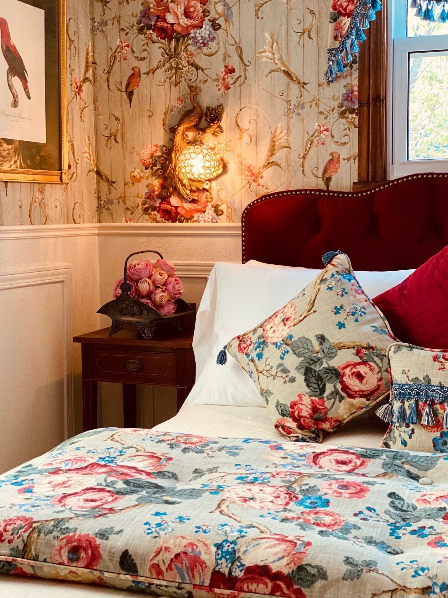 A bedroom with a floral-patterned bedspread, a red upholstered headboard, and a wall with floral wallpaper.