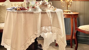 A room with a table set for tea, a lamp, and a view of flowers through a window. - Maison Rose (Hudson)