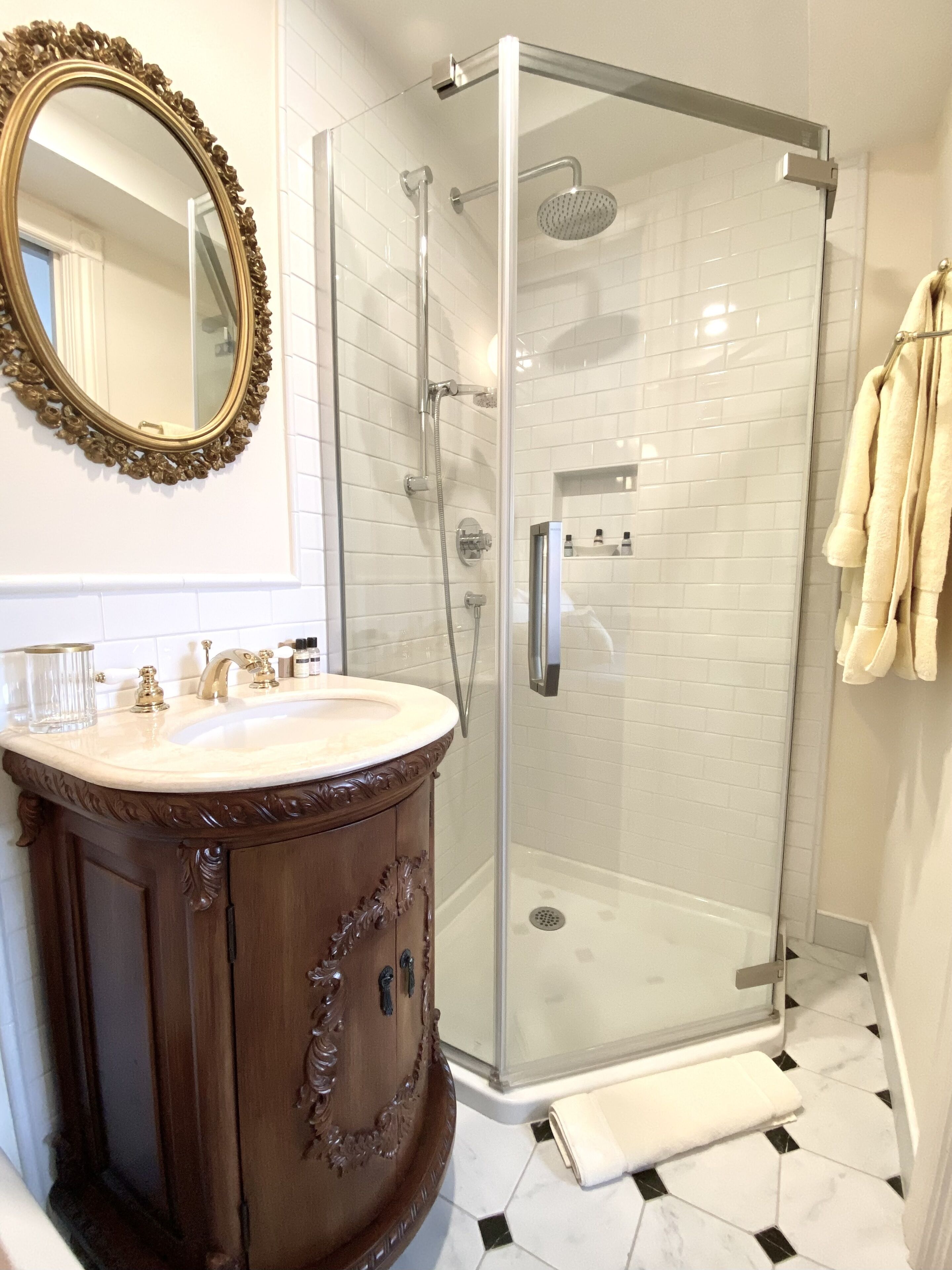 A bathroom with a glass-enclosed shower, a vanity with a mirror, and a tiled floor.