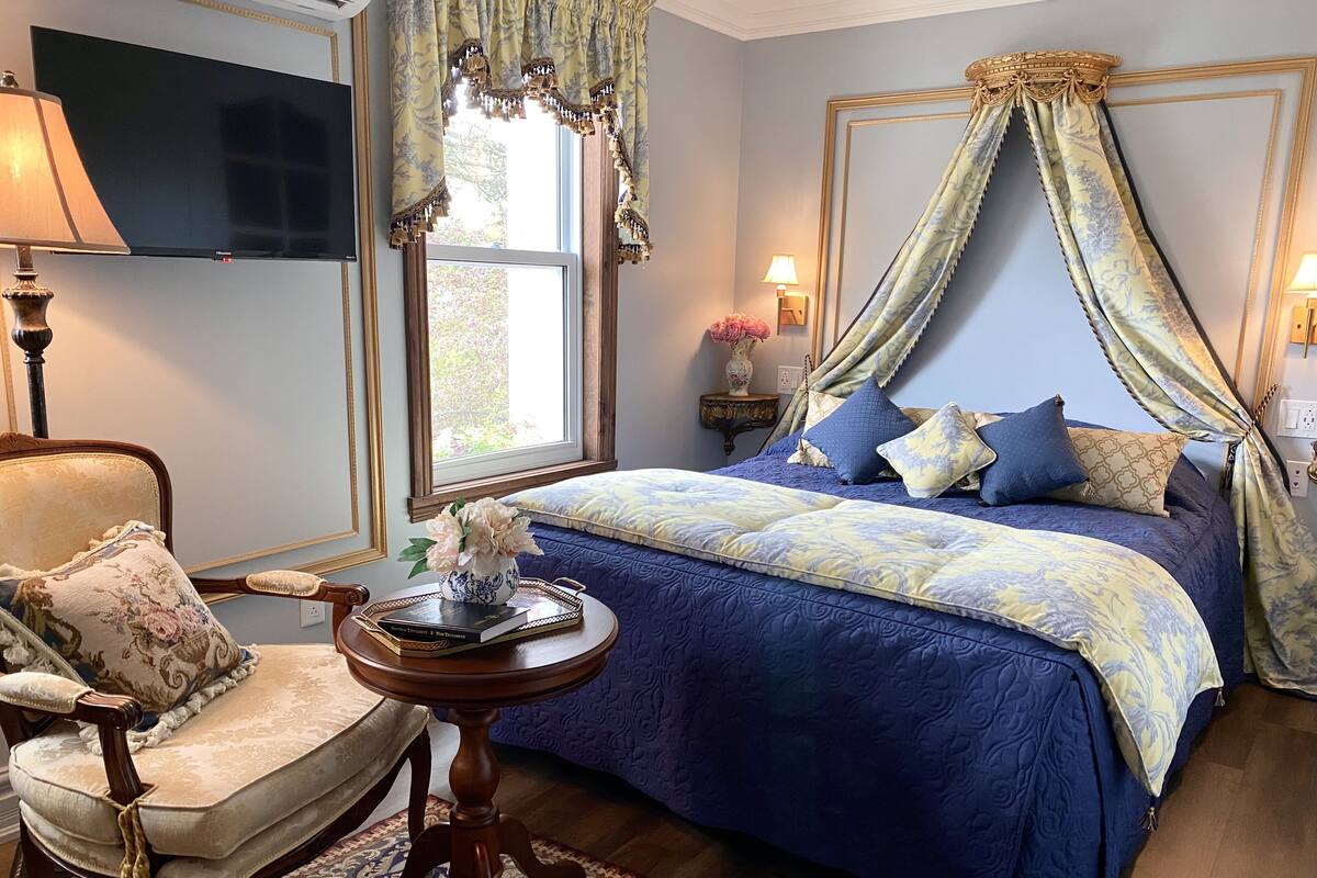 A bedroom with a large bed, a chair, a small table, and a TV.