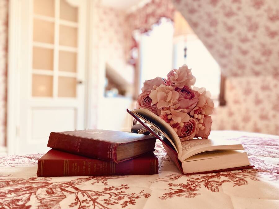 A bed with a floral-patterned bedspread, a stack of books, and a bouquet of flowers.