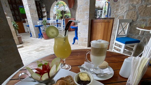 A dining table with a plate of food, including a salad, bread rolls, and a slice of omelette, along with a drink and a cup of coffee.