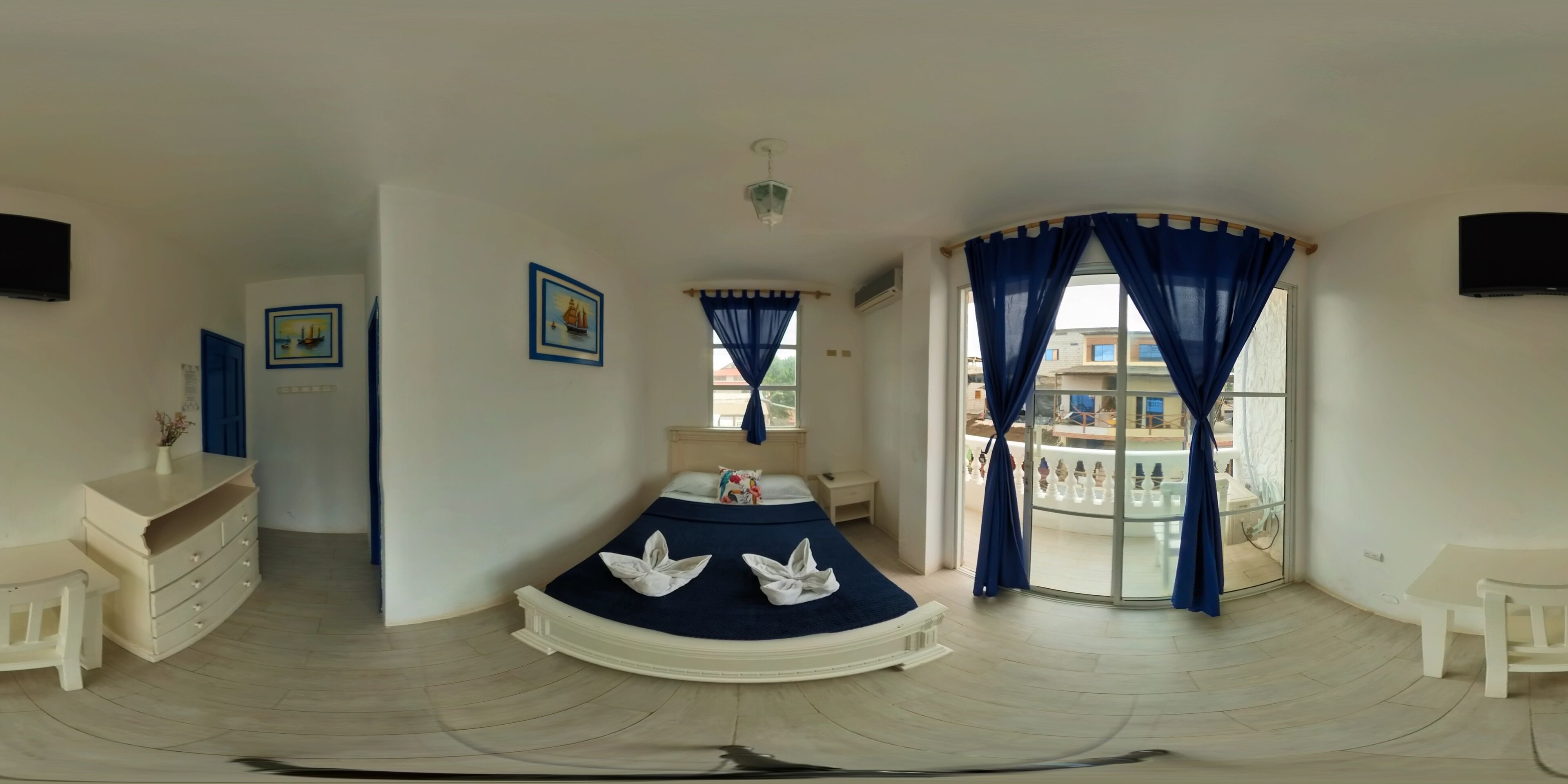 Un dormitorio con una cama curvada, un escritorio, una silla y un balcón con cortinas azules.