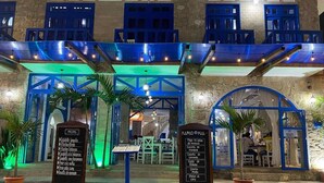 An outdoor dining area with a stone facade, blue accents, and two signboards listing menu items.