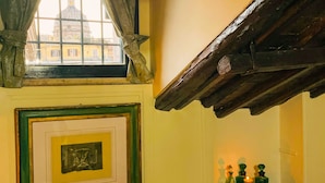 Una habitación con un cuadro enmarcado, una ventana con cortinas y una estantería con botellas.