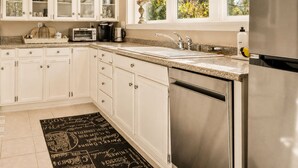 A kitchen with white cabinets, a stainless steel refrigerator, and a window with a view of greenery.
