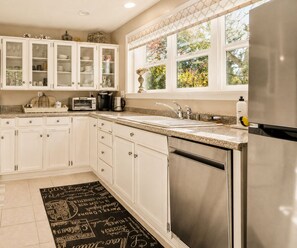 A kitchen with white cabinets, a stainless steel refrigerator, and a window with a view of greenery.