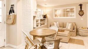 A cozy living room with a round wooden table, wicker chairs, a beige sofa, and a white brick accent wall.