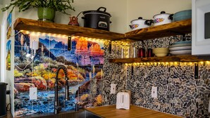 Uma cozinha com painel de parede de pedra, prateleiras de madeira, pia e torradeira.