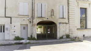A building with a large arched entrance, multiple windows with shutters, and a sign indicating a parking area. - Appartement Ventoux - Welkeys (Avignon)