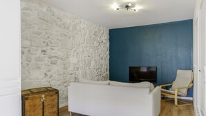 A room with a white sofa, a wooden chest, a television, and a blue wall. - Appartement Ventoux - Welkeys (Avignon)
