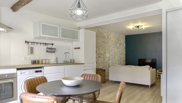 A modern kitchen with white cabinets, a dining area with a round table and leather chairs, and a living room with a sofa and a television. - Appartement Ventoux - Welkeys (Avignon)