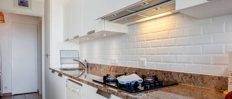 A modern kitchen with white cabinets, a granite countertop, and a stainless steel range hood.