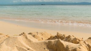 A sandy beach with gentle waves and a boat in the distance. - Escape in the heart of the city Studio Jacuzzis Sauna and swimming pool (Port-Louis)