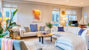 Ein großzügiges Wohnzimmer mit einer großen Eckcouch, einem Couchtisch und einem Fernseher. Übertöpfe und eine Lampe stehen auf einem Beistelltisch.