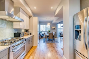 Una cocina moderna con electrodomésticos de acero inoxidable, un comedor con mesa y sillas de madera, y vistas a la ciudad a través de amplios ventanales.