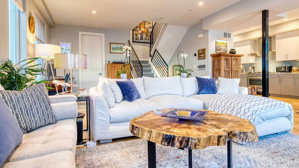 Ein modernes Wohnzimmer mit einem Ecksofa, einem runden Couchtisch und einer Treppe, die in den oberen Bereich führt.
