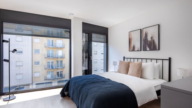 Una camera da letto moderna con un'ampia finestra, un letto con copriletto blu scuro e due quadri appesi al muro.