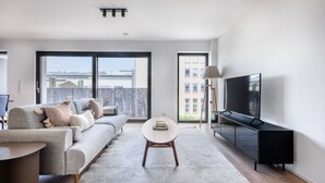 Un soggiorno moderno con un divano grigio, un tavolino rotondo, un mobile TV nero e un'ampia finestra con vista sulla città.