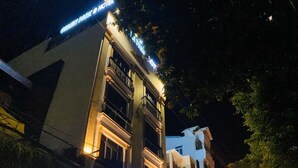 A hotel with a modern facade, illuminated signage, and a parking area with several cars. - Green Park 2 Hotel (Quy Nhon Nam)
