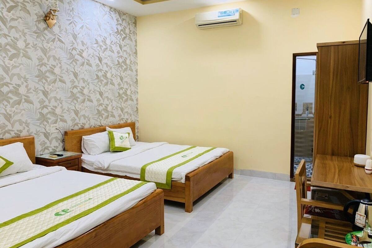 A hotel room with two wooden beds, a wooden desk, a chair, and a wall-mounted air conditioner.