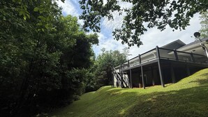 A modern building with a covered outdoor area, surrounded by lush greenery and trees. - Adventure Awaits at Acorn Lane (Pisgah Forest)