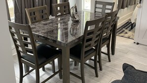 En matplats med ett bord i marmor och stolar i trä, utsikt över omgivningen genom stora fönster och en väggdekoration med marint tema.