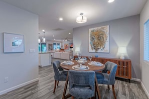 A modern dining area with a round table, blue upholstered chairs, and a large abstract painting on the wall.