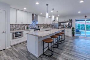 A modern kitchen with a large island, bar stools, stainless steel appliances, and a view to the outside.