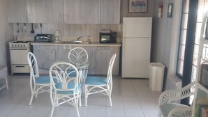 Una cocina con armarios blancos, estufa, microondas y refrigerador. Hay una mesa de comedor con sillas blancas y un ventanal con vistas.