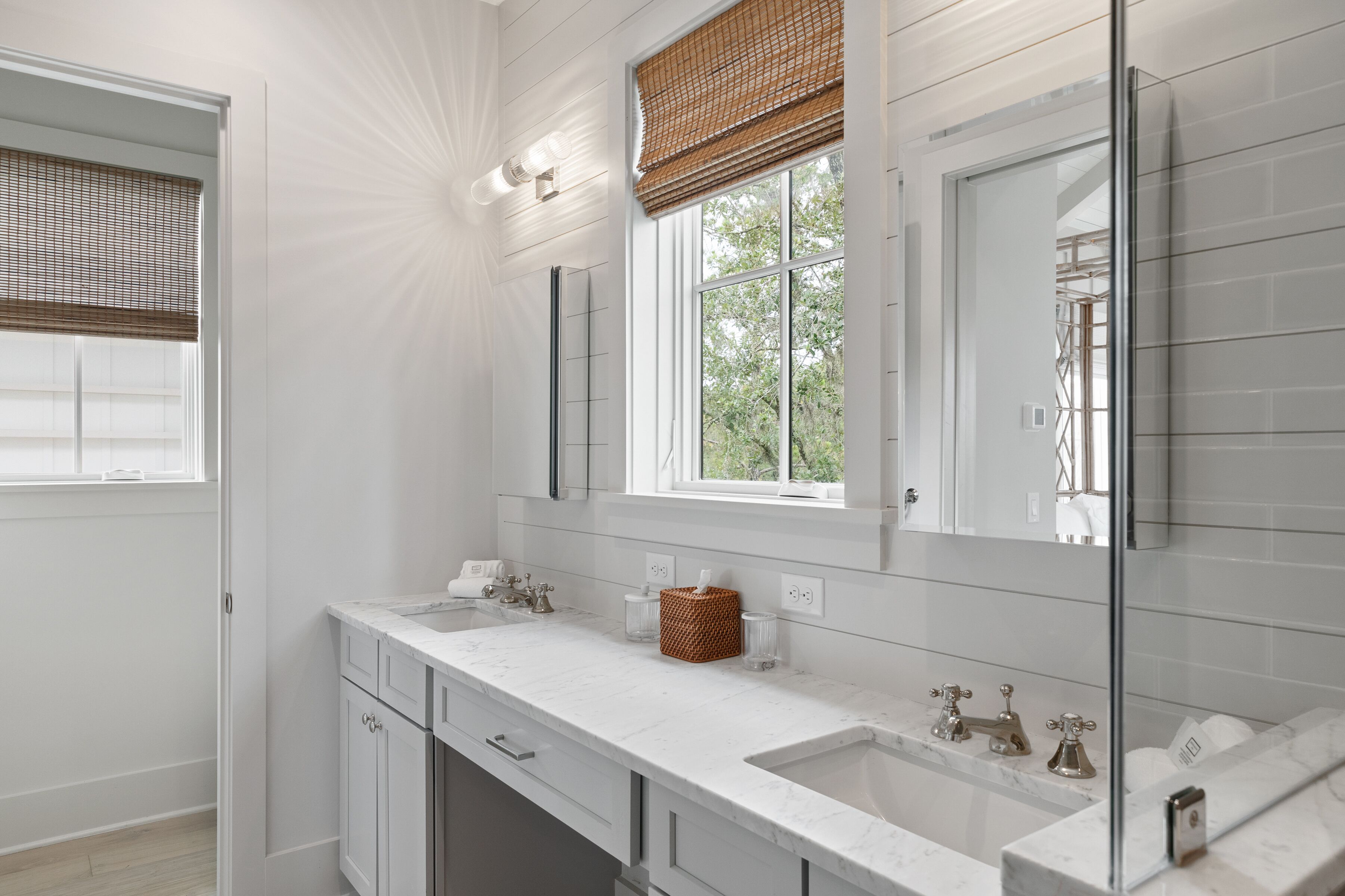 A modern bathroom with white cabinetry, a large mirror, and a window with a view of greenery.