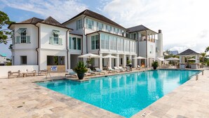 A large, two-story building with a swimming pool, outdoor seating, and a bar area.
