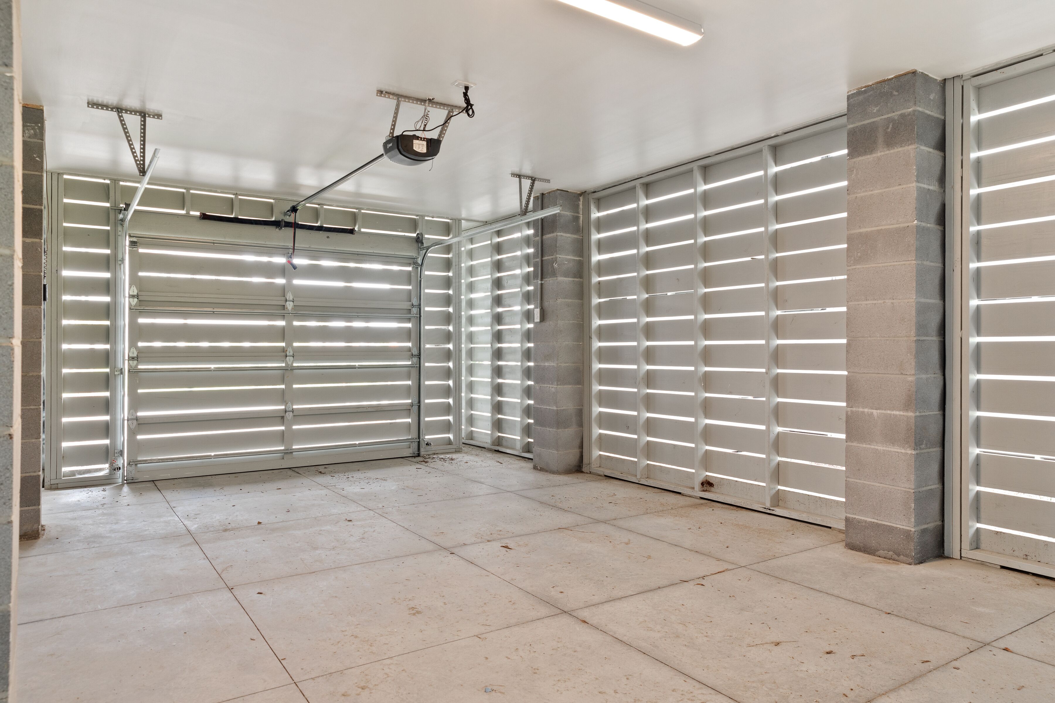 A clean, empty garage with a closed garage door, a ceiling-mounted pulley system, and a tiled floor.