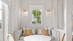 A white room with a round table, a bench with cushions, and a window with a plant.