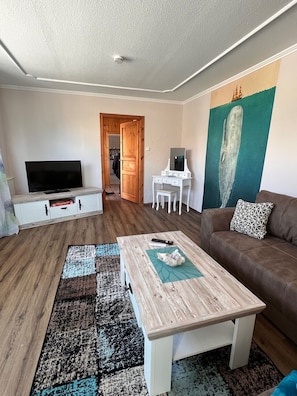A living room with a television, a coffee table, a couch, and a painting on the wall.