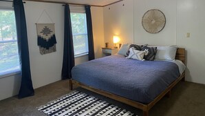 Een slaapkamer met een bed, een plafondventilator, een decoratie aan de muur, een bedlampje en een raam met gordijnen.