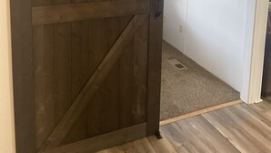 Een houten schuifdeur in de stijl van een schuur in een hal met een tapijten vloer en een witte muur met een klein schilderij.