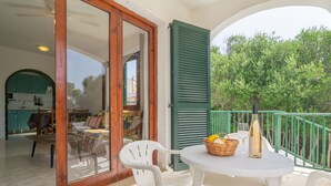 An outdoor patio with a round table, white chairs, a bottle, and a basket of fruit. - BINIFORCAT 11 - Charming apartment with shared pool located 250 meters from the beach. (Ciutadella de Menorca)