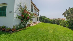 A white building with a green roof and a small porch. There are potted plants along the side of the building. - BINIFORCAT 11 - Charming apartment with shared pool located 250 meters from the beach. (Ciutadella de Menorca)