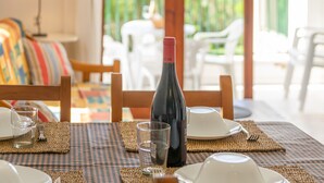 A dining table set with plates, glasses, and a bottle, with a view of a balcony and outdoor furniture. - BINIFORCAT 11 - Charming apartment with shared pool located 250 meters from the beach. (Ciutadella de Menorca)