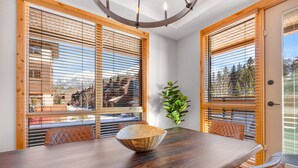 A dining area with a wooden table, a woven bowl centerpiece, and a potted plant. - Spring Creek Vacations 2 BR Premier Condo 107A (Canmore)
