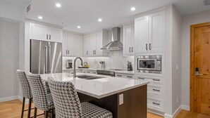 Une cuisine moderne avec des meubles blancs, des appareils en acier inoxydable et un îlot central doté de tabourets de bar.