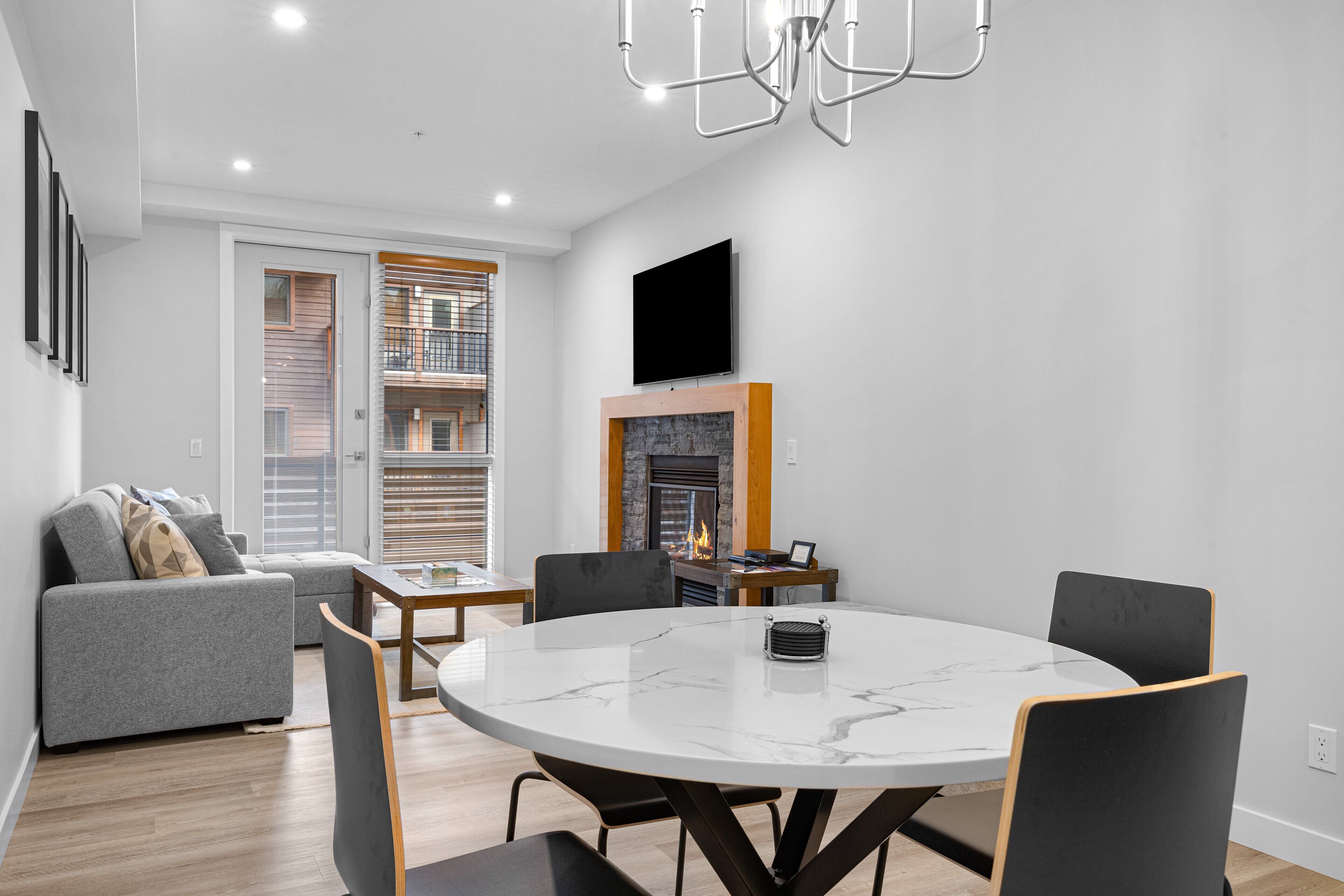 A modern living room with a fireplace, a round dining table, and a grey sofa.