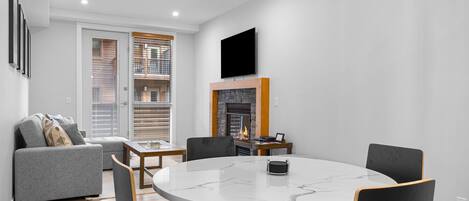 A modern living room with a fireplace, a round dining table, and a grey sofa.