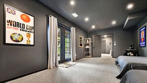 A modern hotel room with a large framed poster of the 1966 World Cup, a large window with curtains, a carpeted floor, and a bed with grey bedding. - Gorgeous Private Apartment (Aliquippa)