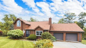 A two-story house with a brick exterior, a chimney, and two garage doors. - Gorgeous Private Apartment (Aliquippa)