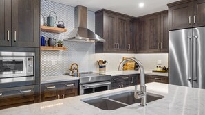 Una cocina moderna con armarios de madera oscura, electrodomésticos de acero inoxidable, un lavamanos grande y un salpicadero con baldosas hexagonales.