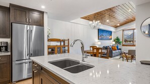 Una cocina moderna con un refrigerador de acero inoxidable, un lavamanos doble, armarios de madera y un comedor con sofá y mesa.
