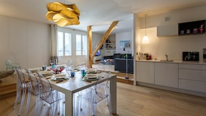 A modern kitchen with white cabinets, a wooden staircase, and a dining area with a wooden table and clear chairs. - Le Majestic 145 appt -  sleeps 6 guests in 3 bedrooms, centre Chamonix, parking (Chamonix)