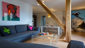 A modern living room with a sofa, coffee table, and a painting. There is a staircase with a wooden railing and a ski-themed wall art. - Le Majestic 145 appt -  sleeps 6 guests in 3 bedrooms, centre Chamonix, parking (Chamonix)
